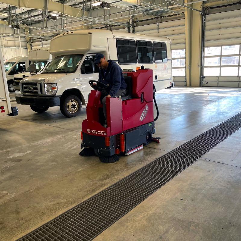 FactoryCat Ride On Floor Scrubbers GTX garage concrete - https://assets.factorycat.com/demoImages/2025/april/GTX-Ride On Floor Scrubbers-garage-concrete-Trenton-USA-825.jpg - 800 - 800 - 825 A FactoryCat GTX battery Ride On Floor Scrubber cleaning the concrete floor of a Trenton, New Jersey transit system garage.