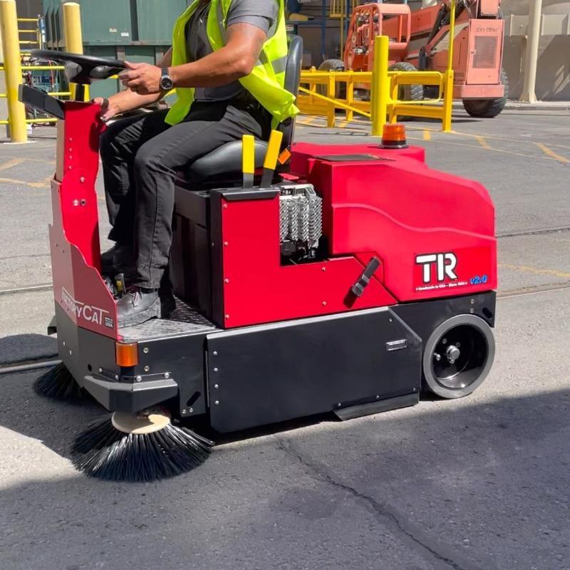 FactoryCat Ride On Floor Sweepers TR loading bays asphalt - https://assets.factorycat.com/demoImages/2025/april/TR-Ride On Floor Sweepers-loading bays-asphalt-San Bernadino-USA-471.jpg - 800 - 800 - 471 A FactoryCat TR battery floor sweeper cleaning the asphalt loading docks outside a fabrication shop in San Bernadino, CA